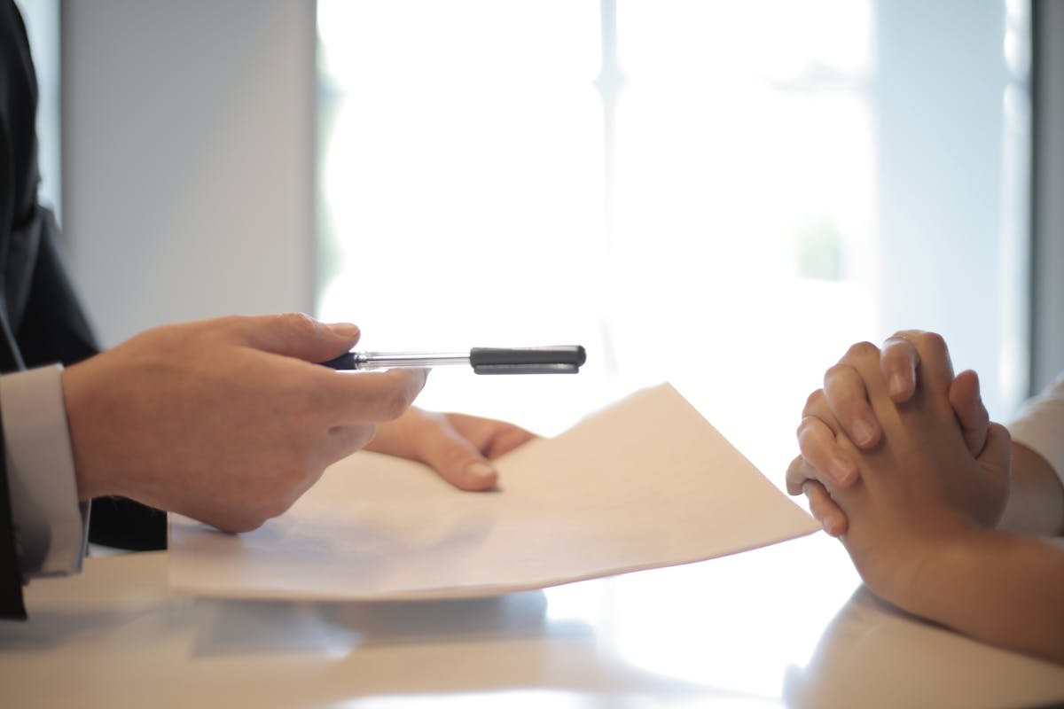 Professional handing over assessment documents at a desk meeting